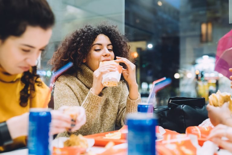 two young women multiethnic indoor eating at fast food - food an